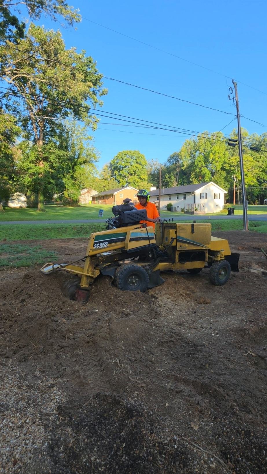 Crew member in a helmet operating a stump grinder in a front yard